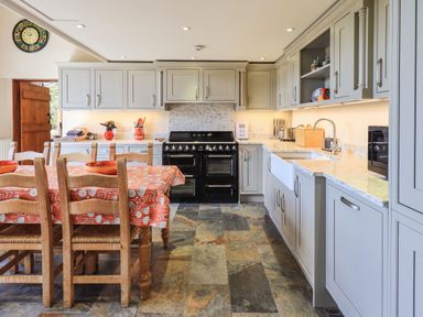 A kitchen with wooden chairs and a table with an orange patterned tablecloth and a black oven at The Stables in Ambleside