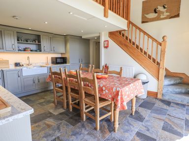 A kitchen with gray cabinets a wooden dining table covered with an orange tablecloth six chairs and wooden staircase at The Stables in Ambleside