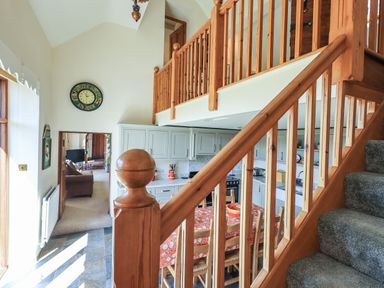 A kitchen with a dining table and chairs next to a staircase with wooden railing and gray carpet at The Stables in Ambleside