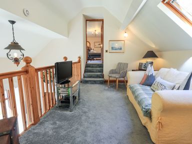 A seating area with a sofa, chair, television on a stand, and carpeted floor at The Stables in Ambleside