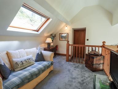A sitting area with a couch under a skylight window a wooden chest and a TV at The Stables in Ambleside