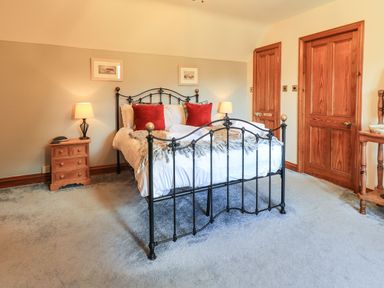 A bedroom with a metal bed frame with white bedding and red pillows and wooden doors and bedside tables with lamps at The Stables in Ambleside