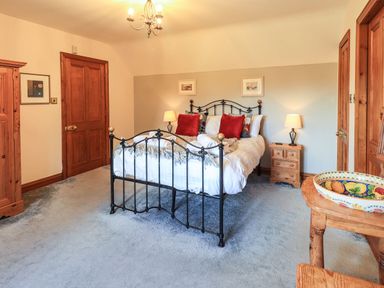 A bedroom with a metal bed frame red pillows wooden doors bedside tables and a wooden table with a decorative bowl at The Stables in Ambleside