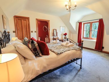 A bedroom with a bed pillows and folded towels a window with red curtains and a chandelier at The Stables in Ambleside