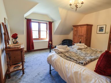 A bedroom with a bed towels on the bed a wooden wardrobe a window with red curtains and a wooden dressing table at The Stables in Ambleside