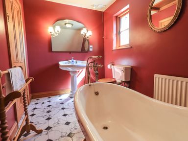 A bathroom with a bathtub sink toilet towel rack mirror and window at The Stables in Ambleside