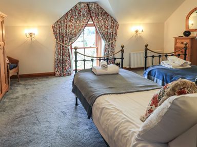A bedroom with two single beds with folded towels a wooden cabinet floral curtains and a wicker chair at The Stables in Ambleside