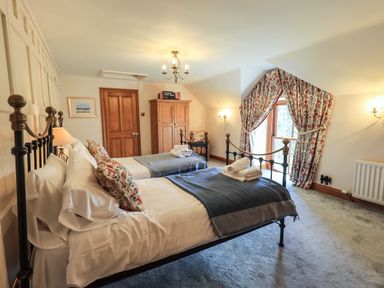 A bedroom with two single beds wooden wardrobe and window with floral curtains at The Stables in Ambleside