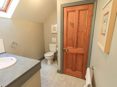 A bathroom with a sink and countertop toilet wooden door and framed pictures on walls at The Stables Ambleside