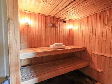 An interior of a wooden sauna with two-tier bench seating and towels folded on the top bench at The Stables in Ambleside
