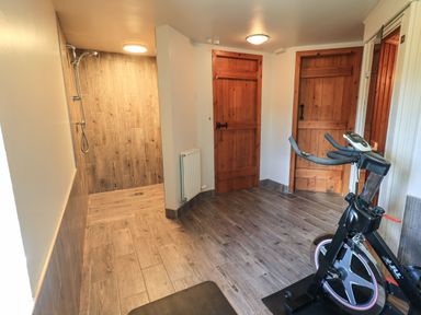 A room with a stationary exercise bike wooden doors and a shower area with wood-look tiles at The Stables in Ambleside