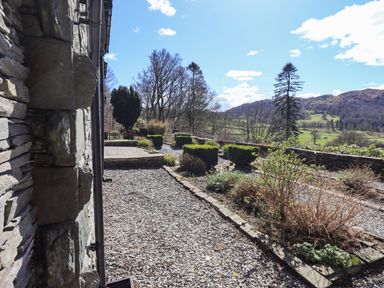 A garden with gravel pathways shrubs and a stone wall overlooking hills and trees at The Stables in Ambleside
