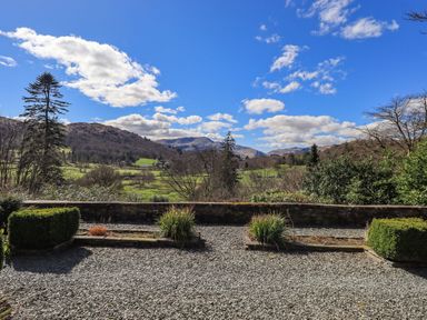 A gravel garden with plants bounded by a low stone wall overlooking hills and trees at The Stables in Ambleside