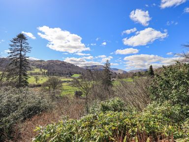 A landscape with trees bushes fields and hills under a blue sky at The Stables in Ambleside