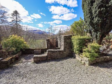 An outdoor garden area with stone walls and gravel ground with shrubs and trees at The Stables in Ambleside