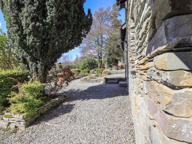 A gravel pathway beside a stone wall with trees and bushes at The Stables in Ambleside
