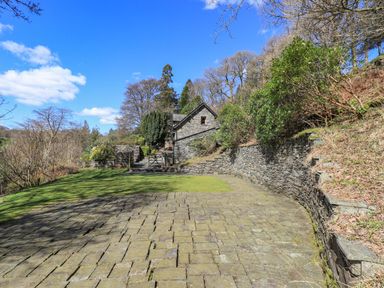 A stone paved courtyard with a stone house and garden walls surrounded by trees and shrubs at The Stables in Ambleside