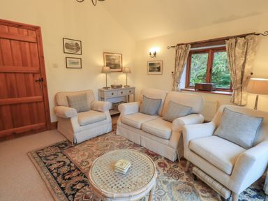 A living room with two armchairs a sofa a round coffee table a wooden door and a window with curtains at Hannakin Barn Hawkshead