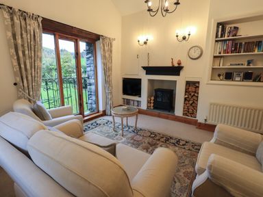 A living room with beige sofas a fireplace built in bookshelves and glass doors at Hannakin Barn in Hawkshead