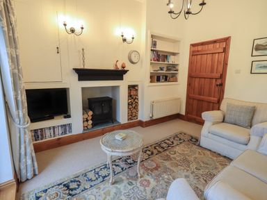 A living room with a fireplace wood stove bookshelf sofa armchair and wooden door at Hannakin Barn in Hawkshead