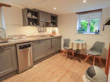A kitchen with gray cabinets stainless steel dishwasher small round table with two gray chairs and a window with a herb planter at Hannakin Barn in Hawkshead