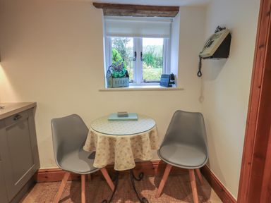A small dining area with two gray chairs and a round table under a window with a plant and a device at Hannakin Barn in Hawkshead