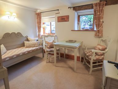 A sitting area with a small table and two chairs near windows and a cushioned bench with pillows at Hannakin Barn in Hawkshead
