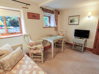A sitting area with two chairs and a table next to a couch with cushions and a small TV on a stand at Hannakin Barn in Hawkshead