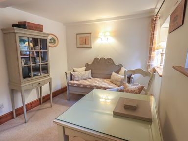 A sitting area with a cushioned bench sofa and glass top table with chair at Hannakin Barn in Hawkshead