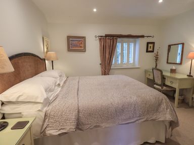 A bedroom with a large bed two bedside lamps a window with curtains and a desk with a mirror and chair at Hannakin Barn in Hawkshead