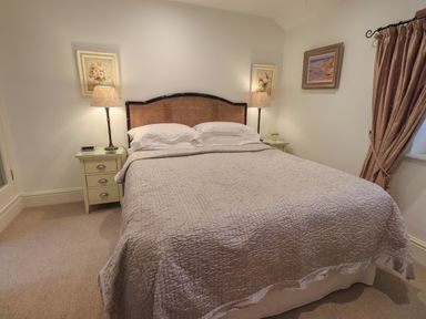 A bedroom with a double bed between two bedside tables with lamps and paintings on the walls at Hannakin Barn in Hawkshead