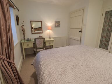 A bedroom with a bed, a desk with a chair, a lamp, and curtains at Hannakin Barn in Hawkshead