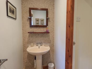 A small bathroom with a pedestal sink mirror and shelf at Hannakin Barn in Hawkshead