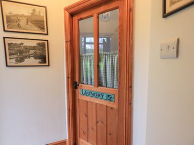 A wooden door with glass panels and a sign reading laundry 15 cents in a hallway with framed pictures on the wall at Hannakin Barn in Hawkshead