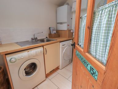 A laundry room with a washing machine sink dryer and a wooden door with a laundry sign at Hannakin Barn in Hawkshead