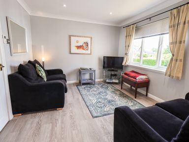 A living room with black sofas a small table a television and a window with curtains at Fairview in Bowness