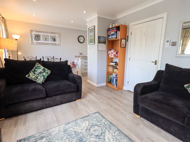 A living room with two black sofas a green patterned cushion a wooden bookshelf and a wall clock at Fairview in Bowness