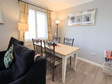 A dining area with a wooden table and four metal chairs next to a black sofa with patterned cushions at Fairview in Bowness