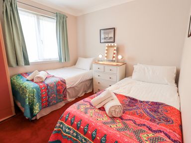 A bedroom with two beds with colorful bedspreads a window with curtains a white dresser with a mirror and lamps