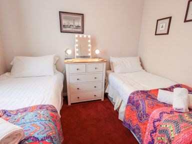 A bedroom with two single beds with white bedding and colorful blankets a white chest of drawers with lights and lamps on top at Fairview in Bowness