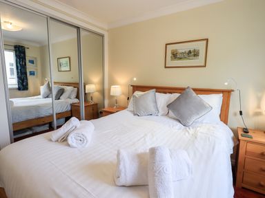 A bedroom with a double bed with rolled white towels and two grey pillows a mirrored wardrobe a bedside table with a lamp and a painting on the wall at Fairview in Bowness