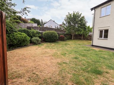 A yard with grass bushes and trees next to a white house at Fairview in Bowness