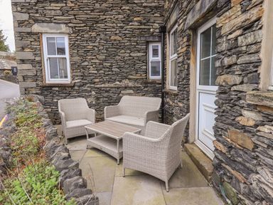 A stone exterior seating area with wicker chairs and a table outside a building at Gildabrook Cottage in Bowness
