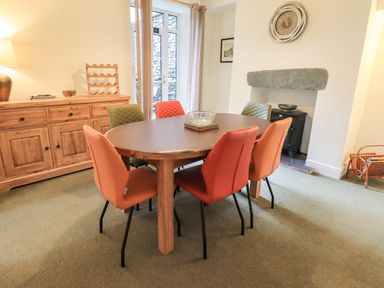 A dining room with a round wooden table and six colorful chairs by a wooden sideboard and French doors at Gildabrook Cottage in Bowness