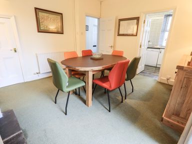 A dining room with a round table and six chairs in green and orange at Gildabrook Cottage in Bowness