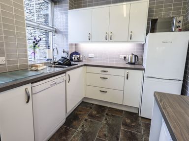 A kitchen with white cabinets a dishwasher a sink a kettle a fridge and a microwave at Gildabrook Cottage in Bowness
