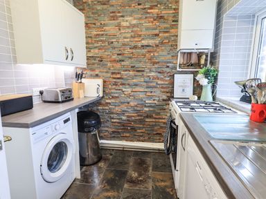 A kitchen with a washing machine toaster sink stove and trash bin at Gildabrook Cottage in Bowness