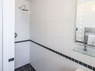 A tiled bathroom shower area with a rain showerhead a towel rack and a mirror with lights at Gildabrook Cottage in Bowness