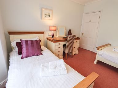 A bedroom with two single beds a desk with a lamp and chair and a closed door at Gildabrook Cottage in Bowness