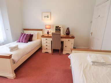 A bedroom with two single beds a desk with a lamp and a chair at Gildabrook Cottage in Bowness